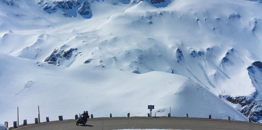 Motorradfahrer in einer Kehre der Grossglockner Hochalpenstraße, mit Blick auf schneebedeckte Berge
