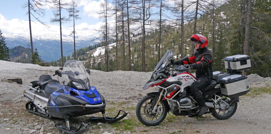 Motorradfahrer an der Tauplitzalmstraße, neben einem Schneemobil im Wald