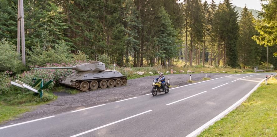 Motorradfahrer auf dem Wurzenpass im Wald, mit Ausstellungspanzer im Hintergrund 