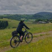 Frau fährt Ebike durch Mittelgebirgslandschaft in Deutschland
